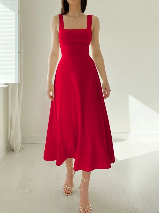Frau trägt ein leuchtend rotes ärmelloses Midikleid mit tailliertem Oberteil und weitem Rock.